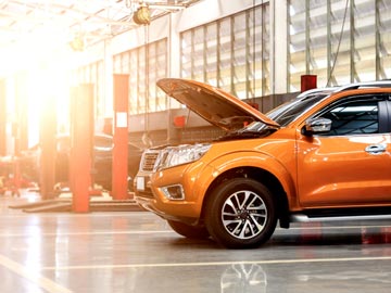 Ein orangefarbenes SUV steht in einer gut beleuchteten Auto-Werkstatt bei Autoankauf Ingolstadt, dessen Motorhaube offen ist und den Motor zeigt.